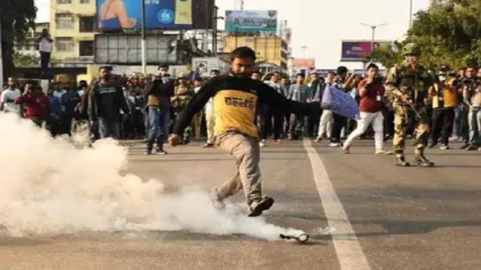नागरिकता विधेयक के खिलाफ हिंसा के दौरान आँसू गैस के गोले को लात मारता प्रदर्शनकारी (TOI से साभार)